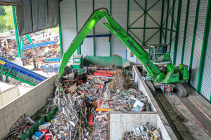  Der Umschlagbagger SENNEBOGEN 830 E-Serie in der Raupenvariante belädt die Schere mit 17 m-Ausrüstung in einer halboffenen Halle  